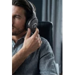 Close-up of a man wearing large over-ear headphones, adjusting the right earcup with his hand.