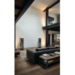 Modern living room with tall black metal beams, two gray floor speakers, and a dark leather sectional around a wooden coffee table with books.