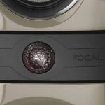 Close-up of a black speaker grille with a geometric lattice dome, the word FOCAL embossed on the dark panel nearby, beige surfaces above and below.
